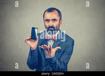 Closeup Portrait bärtigen ernste frustriert, Geschäftsmann, tragen, elegante Jacke mit roter Fliege, zeigt seine Telefon- und deutete mit seinem anderen han Stockfoto