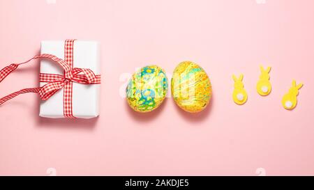 Ostern Eier, weiße Geschenkbox mit roten Geschenk Bug und gelbe Kaninchen auf rosa Hintergrund. Flach Draufsicht Ostern Konzept Stockfoto