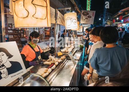 Eine Frau grillt an einem Lebensmittelstand im Shi Lin Night Market, Taipei, Taiwan, für eine Schlange von Kunden die Pilze aus der Austernzucht Stockfoto