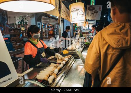 Eine Frau grillt an einem Lebensmittelstand im Shi Lin Night Market, Taipei, Taiwan, für eine Schlange von Kunden die Pilze aus der Austernzucht Stockfoto