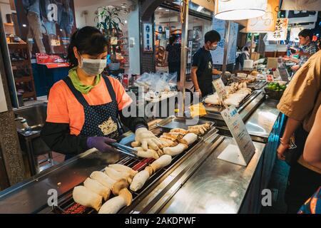 Eine Frau grillt an einem Lebensmittelstand im Shi Lin Night Market, Taipei, Taiwan, für eine Schlange von Kunden die Pilze aus der Austernzucht Stockfoto