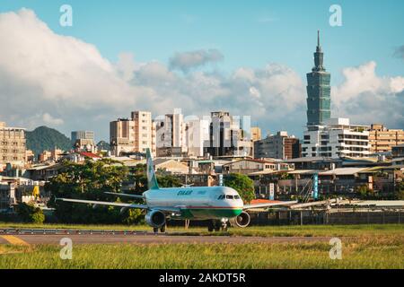 Ein EVA Air Airbus A321 wird an einem sonnigen Abend am Songshan Airport in Taipeh zum Start gebracht. Dahinter ist der Wolkenkratzer Taipei 101 zu sehen Stockfoto