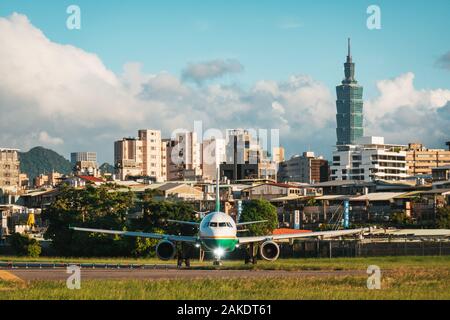 Ein EVA Air Airbus A321 wird an einem sonnigen Abend am Songshan Airport in Taipeh zum Start gebracht. Dahinter ist der Wolkenkratzer Taipei 101 zu sehen Stockfoto