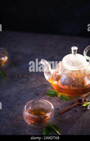 Teekanne aus Glas mit Doppelwand Glas Schalen auf einem Stein Hintergrund mit Tee Blätter Stockfoto