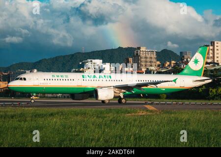 Ein EVA Air Airbus A321 wird an einem sonnigen Abend am Songshan Airport in Taipeh zum Start gebracht. Dahinter ist ein Regenbogen zu sehen Stockfoto