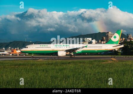 Ein EVA Air Airbus A321 wird an einem sonnigen Abend am Songshan Airport in Taipeh zum Start gebracht. Dahinter ist ein Regenbogen zu sehen Stockfoto