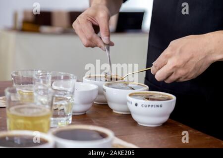 Professional Q Sortierer Vorbereitung zu testen und die Kontrolle der Qualität des Kaffees und der kaffeesatz aus Keramik Schale auf dem Tisch abschöpfen. Stockfoto