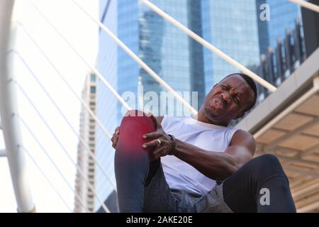 Afrikanische amerikanische Sportler verwendet zwei Hände halten sein Knie nach Gefühl, Schmerz und Verletzung in Hart ausgeführt. Gesundheit, Sport und ich Stockfoto