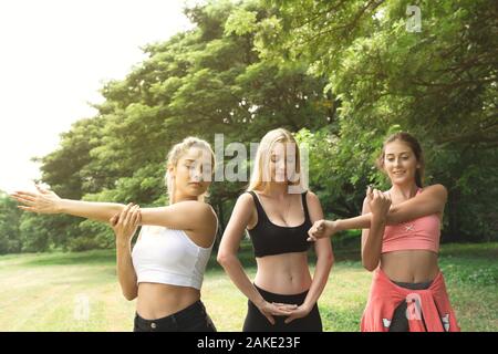 Glücklichen gesunden drei schöne junge Teenager Frau Training und Stretching für das Aufwärmen vor dem Training im Park. Fitness, Sport, Freundschaft und Stockfoto