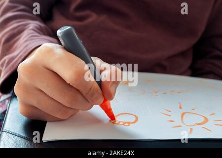 Junger Teenager mit einem orangen Farbe textmarker, die Blume und die Sonne cartoon Symbol auf dem Papier im Klassenzimmer. Bildung und Schule anhand von quantitativen Simulatio Stockfoto