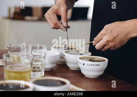 Professional Q Sortierer Vorbereitung zu testen und die Kontrolle der Qualität des Kaffees und der kaffeesatz aus Keramik Schale auf dem Tisch abschöpfen. film Stil Stockfoto