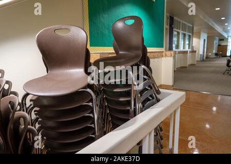 Zwei Reihen von Braun stapelbare Stühle an einer Schule Einstellung unter Treppe gestapelt Stockfoto