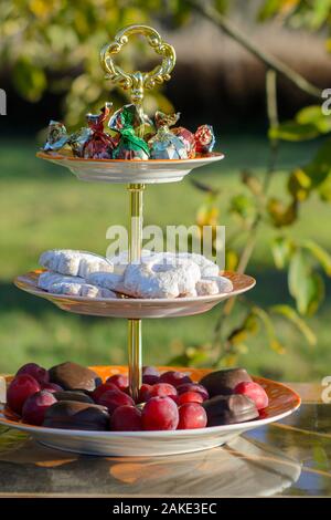 Pflaumen, Kekse und Süßigkeiten auf einem Ständer im Garten. Outdoor. Stockfoto