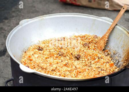 Pilav in Kessel. Eine köstliche Pilav mit Schweinefleisch, Karotten und Reis mit scharfer Gewürze und Zwiebeln, in einem Kessel mit einem Holzspachtel entfernen. Close-up. Stockfoto