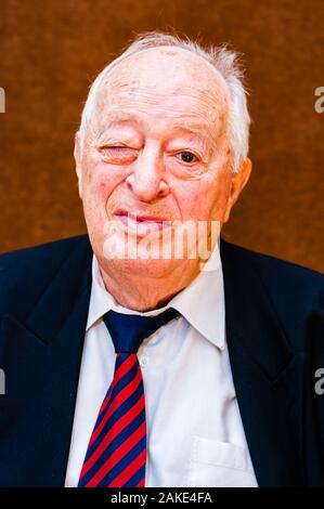 Portrait von positiven weißen älteren Mann mit dunkler Anzug, weißes Hemd und Krawatte gestreift blau rot zwinkerte mit einem Auge auf hellen braunen Hintergrund Stockfoto