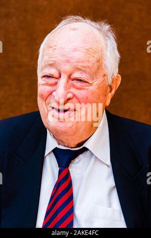 Portrait von Happy white älterer Mann mit dunkler Anzug, weißes Hemd und Krawatte gestreift blau rot Lächeln auf hellen braunen Hintergrund Stockfoto