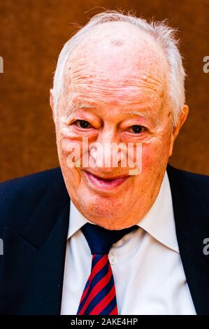 Portrait von Happy white älterer Mann mit dunkler Anzug, weißes Hemd und Krawatte gestreift blau rot Lächeln auf hellen braunen Hintergrund Stockfoto