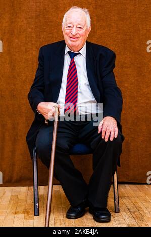 Portrait von Happy white älterer Mann mit dunkler Anzug, weißes Hemd und Krawatte gestreift Blau Rot lächelnd saß auf einem Stuhl und halten die Hand auf wenige Stic Stockfoto