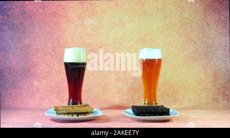 Zwei hohe Gläser mit den hellen und dunklen Bier mit weißer Schaum vor zwei Platten mit Weizen und Roggen Croutons. Close-up. Stockfoto