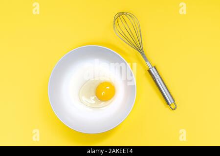 Ein Ei in die Schüssel mit einem Schläger auf einem gelben Oberfläche Stockfoto