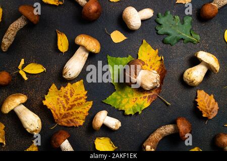 Herbst Hintergrund mit Pilzen und Blätter. Pilze Steinpilze, orange-cap Steinpilzen und Herbstlaub auf braunen Tisch. Pilze Muster, flach Stockfoto