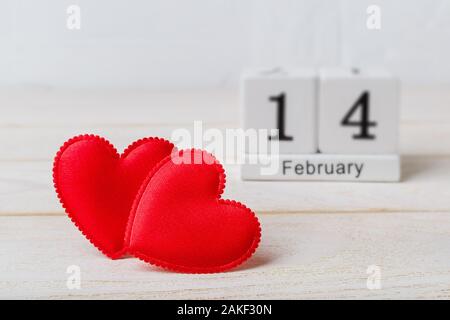 Zwei rote Seide Valentine Herzen und Holz- ewiger Kalender mit Datum vom 14. Februar auf einem weißen Holz- strukturierten Hintergrund. Konzept Liebe, Valentinstag Stockfoto