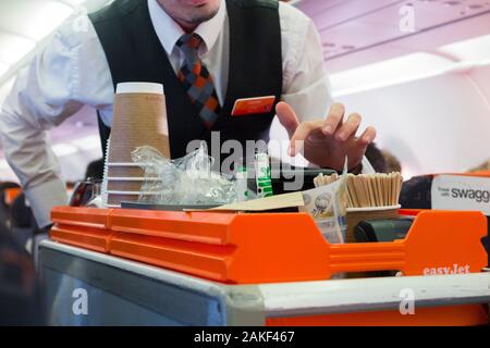 Kabinenbesatzung/Luftsteward serviert Passagieren von einem Rollwagen während eines Easyjet-Flugs auf einem Airbus-Flugzeug Getränke und Snacks. (115) Stockfoto