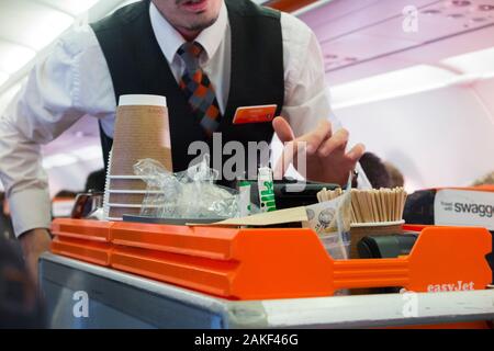 Kabinenbesatzung/Luftsteward serviert Passagieren von einem Rollwagen während eines Easyjet-Flugs auf einem Airbus-Flugzeug Getränke und Snacks. (115) Stockfoto