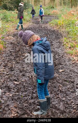 Mutter/Mutter/Mutter/Mutter, die mit ihren drei Kindern an einem Wintertag auf einem schlammigen Weg durch Wälder auf West End Common, Esher, Surrey durch den Schlamm spazieren. GROSSBRITANNIEN. (115) Stockfoto