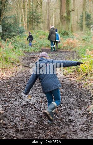 Mutter/Mutter/Mutter/Mutter, die mit ihren drei Kindern an einem Wintertag auf einem schlammigen Weg durch Wälder auf West End Common, Esher, Surrey durch den Schlamm spazieren. GROSSBRITANNIEN. (115) Stockfoto