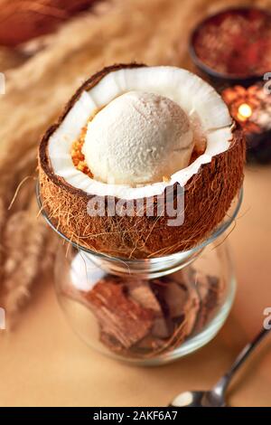 Teil der leckeres Eis mit Muttern und Zitronensauce in halbierten Kokosnuss. In Glas mit crushed Kokosnussschalen diente, auf beigem Hintergrund. Stockfoto