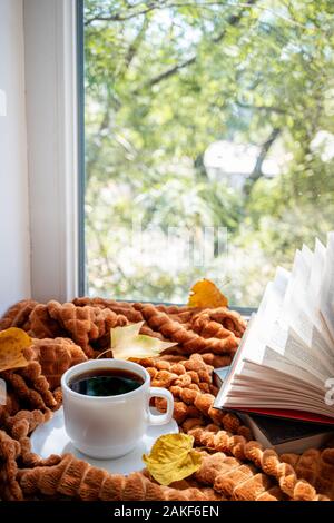 Kaffeetasse, offene Bücher, warmes Plaid und Herbstliche Blätter auf einer Fensterbank im Herbst. Herbst Hintergrund. Gemütliches Heim, Kaffeepause, hygge, Lesen, Startseite co