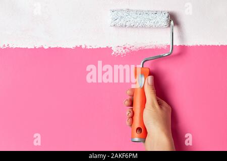 Weibliche hand Malen mit Bürstenrolle rosa Oberfläche in weißer Farbe. Stockfoto