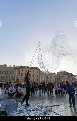 Die Menschen beobachten, wie ein Mann im Rynek Glowny (Hauptmarktplatz) im Zentrum von Krakow (Krakow), Polen, riesige Blasen erzeugt Stockfoto