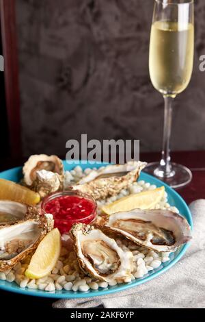 Platte mit halben Dutzend von frischen Austern geöffnet, mit Soße und Zitrone auf weißen Steine und hohes Glas Champagner auf Holztisch. Stockfoto