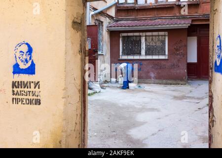 Ein Arbeiter in einem Hof, der eine blaue Arbeitskleidung trägt, wird von blauen Graffiti an der Außenwand in Lemberg, Ukraine, umrahmt Stockfoto