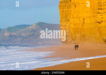 Burton Bradstock, Dorset, Großbritannien. 9. Januar 2020. UK Wetter. Spaziergänger Flanieren zwischen dem Waschen von den brechenden Wellen und die Klippen an einem sonnigen Morgen im Hive Strand bei Burton Bradstock in Dorset. Foto: Graham Jagd-/Alamy leben Nachrichten Stockfoto