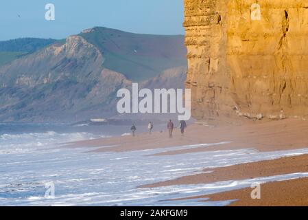 Burton Bradstock, Dorset, Großbritannien. 9. Januar 2020. UK Wetter. Spaziergänger Flanieren zwischen dem Waschen von den brechenden Wellen und die Klippen an einem sonnigen Morgen im Hive Strand bei Burton Bradstock in Dorset. Foto: Graham Jagd-/Alamy leben Nachrichten Stockfoto