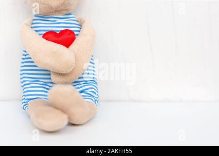 Plüsch Spielzeug Bär Holding rotes Herz in der Hand auf dem weißen Hintergrund mit der Liebe. Valentinstag. Konzept der Liebe und darauf warten, dass jemand. Stockfoto
