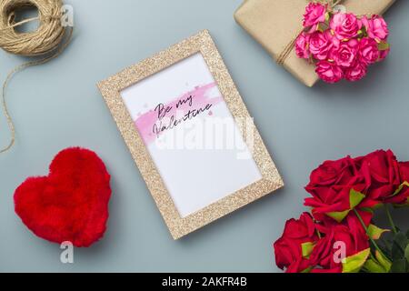 Mockup goldenen Bilderrahmen für Valentines Tag Konzept. Blick von oben auf die Mock up Bilderrahmen mit rosa Blüten, Handwerk Rosen, praktische Fertigkeit Geschenkbox auf Grau h Stockfoto