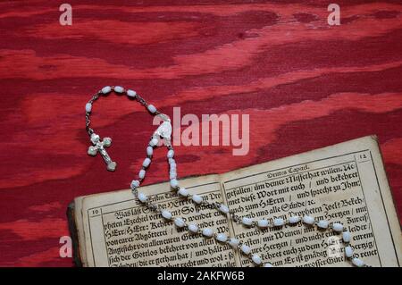 Rosary mit sehr altem altem Buch in altdeutscher Schrift auf rotem Holztisch Stockfoto