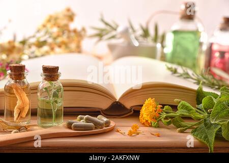 Die traditionelle Medizin für die Herstellung von Arzneimitteln, die mit Kapseln und heilenden Essenzen und Rezeptbuch auf hölzernen Tisch. Vorderansicht. Panoramablick gesundes Stockfoto