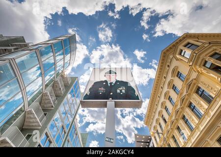 Weitwinkelansicht von unten am Checkpoint Charlie in Berlin, mit dem Bild des amerikanischen Soldaten in der Mitte, gegen eine blaue Sommerwolkenlandschaft Stockfoto