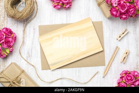 Mockup leer Holz- Karte und Umschlag auf grunge weißem Holz mit Kraftpapier Rosen und Handarbeit Handwerk Geschenk zum Valentinstag. Mock up für elegante Stockfoto