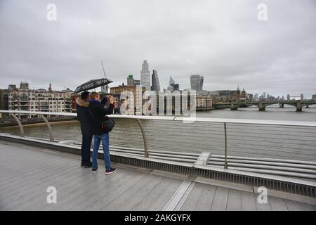 London, Großbritannien, 9. Januar 2020, Wetter. Dunkler Nachmittag in der Stadt, wenn starker Regen kommt. Ein Paar, das unter einem Regenschirm steht und ein Foto auf der Millennium Bridge fotografiert Stockfoto