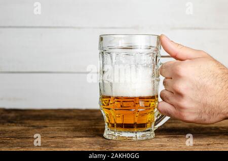 Männliche hand mit einem halb vollen Glas Bier mit Schaum auf Holztisch. Platz kopieren Stockfoto