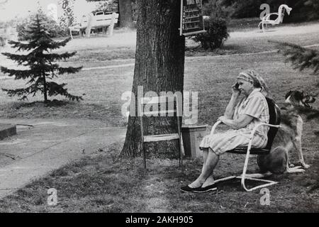 Schöne Siebziger Schwarz-Weiß-Fotografie einer älteren Frau und ihres großen Hundes, der in einem Park sitzt Stockfoto