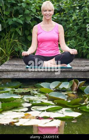 Portrait von reife Frau in Yoga Position auf hölzernen Steg am See Stockfoto