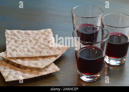 Das Abendmahl des Herrn mit ungesäuertem Brot und drei kleinen Kelchen Wein auf einem zyanfarbenen Holztisch Stockfoto