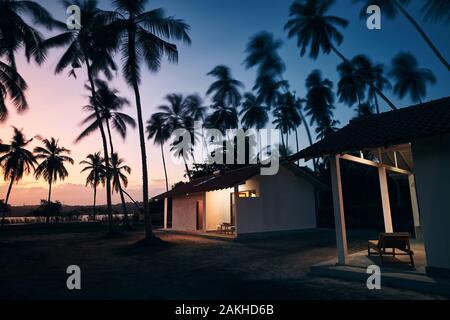 Tourist Resort in tropischen Ziel. Bungalows unter Kokospalmen in der Nähe der Lagune bei Sonnenuntergang. Stockfoto